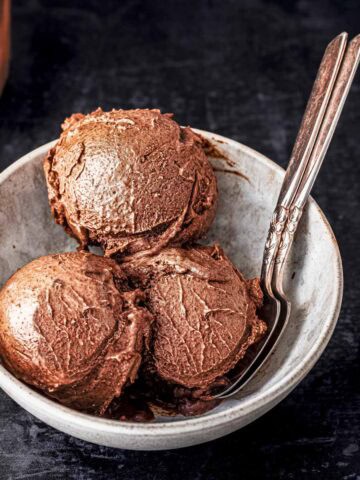 Three scoops of Ninja creami chocolate ice cream served in a white bowl and 2 spoons.