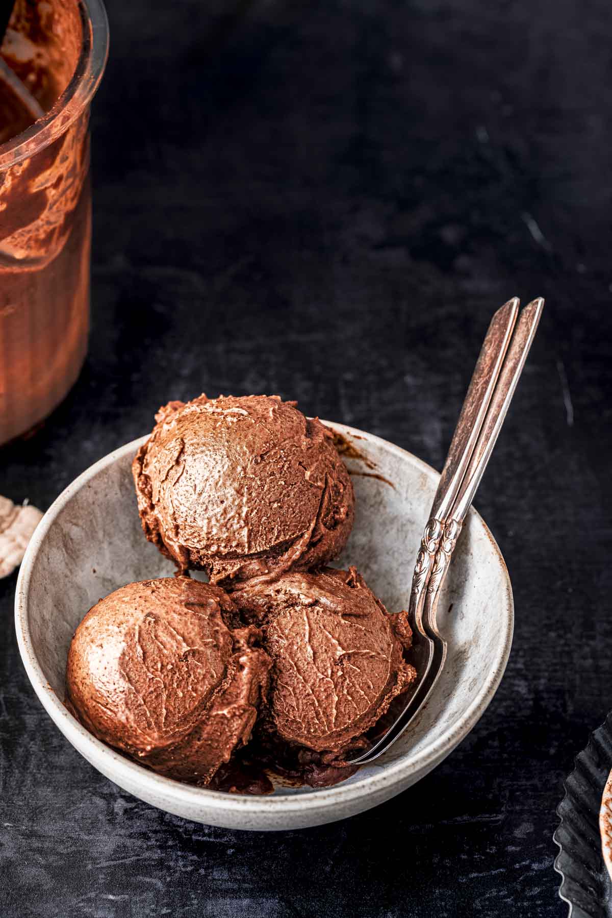 Three scoops of Ninja creami chocolate ice cream served in a white bowl and 2 spoons.