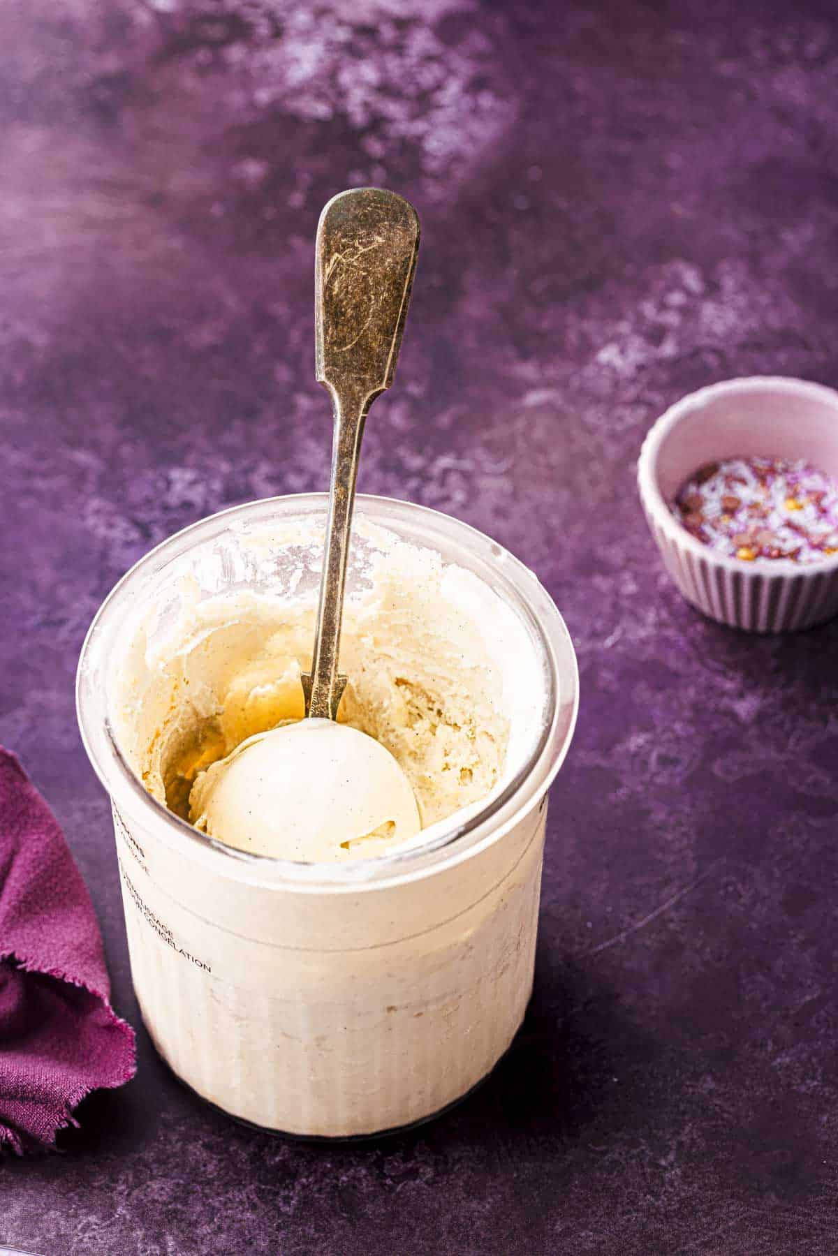 NInja creami frozen yogurt in pint tub with a spoon and sprinkles in a pink cup.