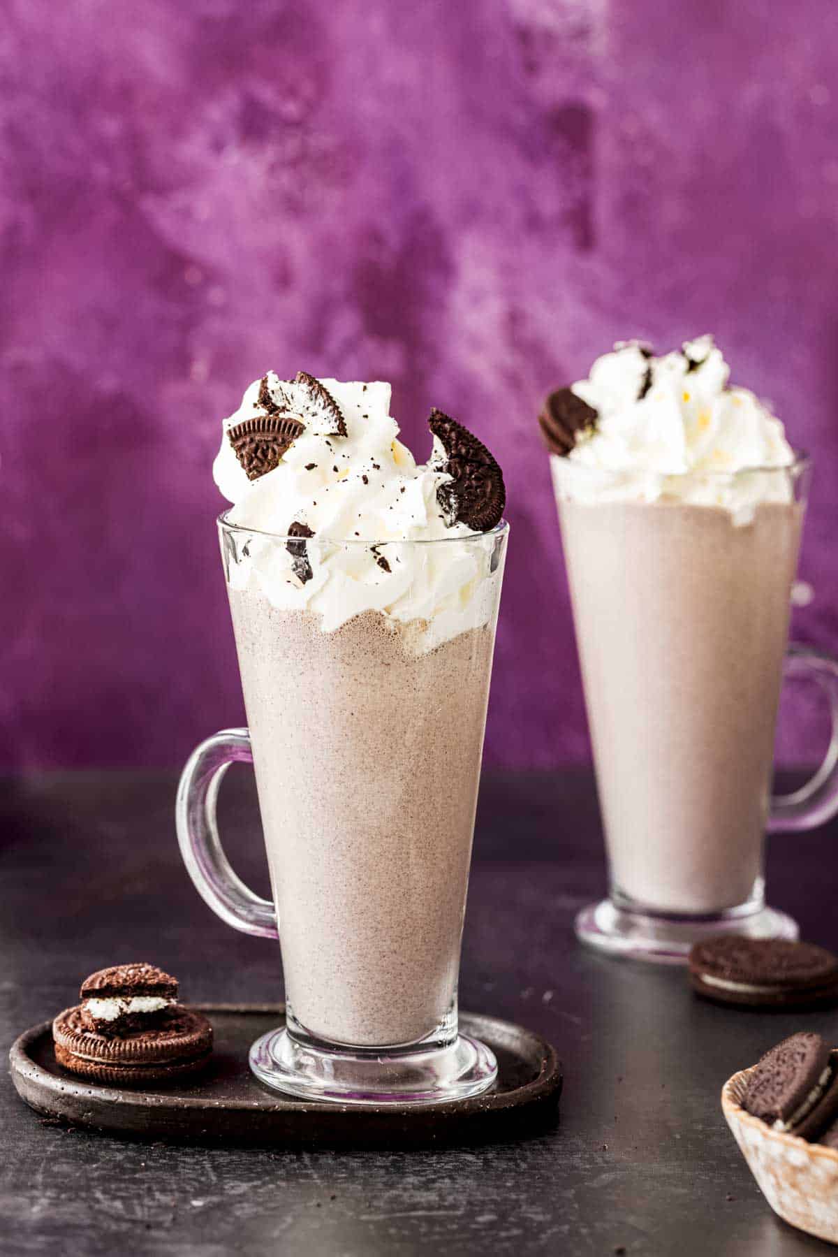 two glasses of cookies and cream milkshake topped with whipped cream and oreo cookies.