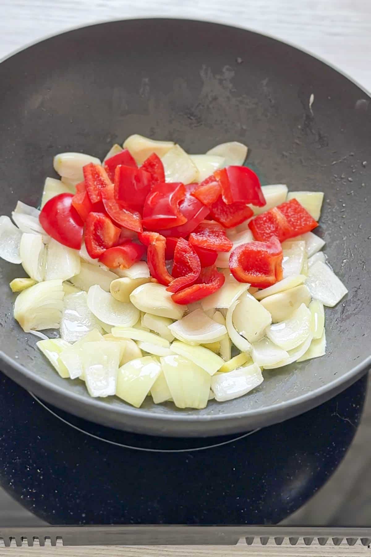 red pepper on top of onion ginger garlic in a wok.