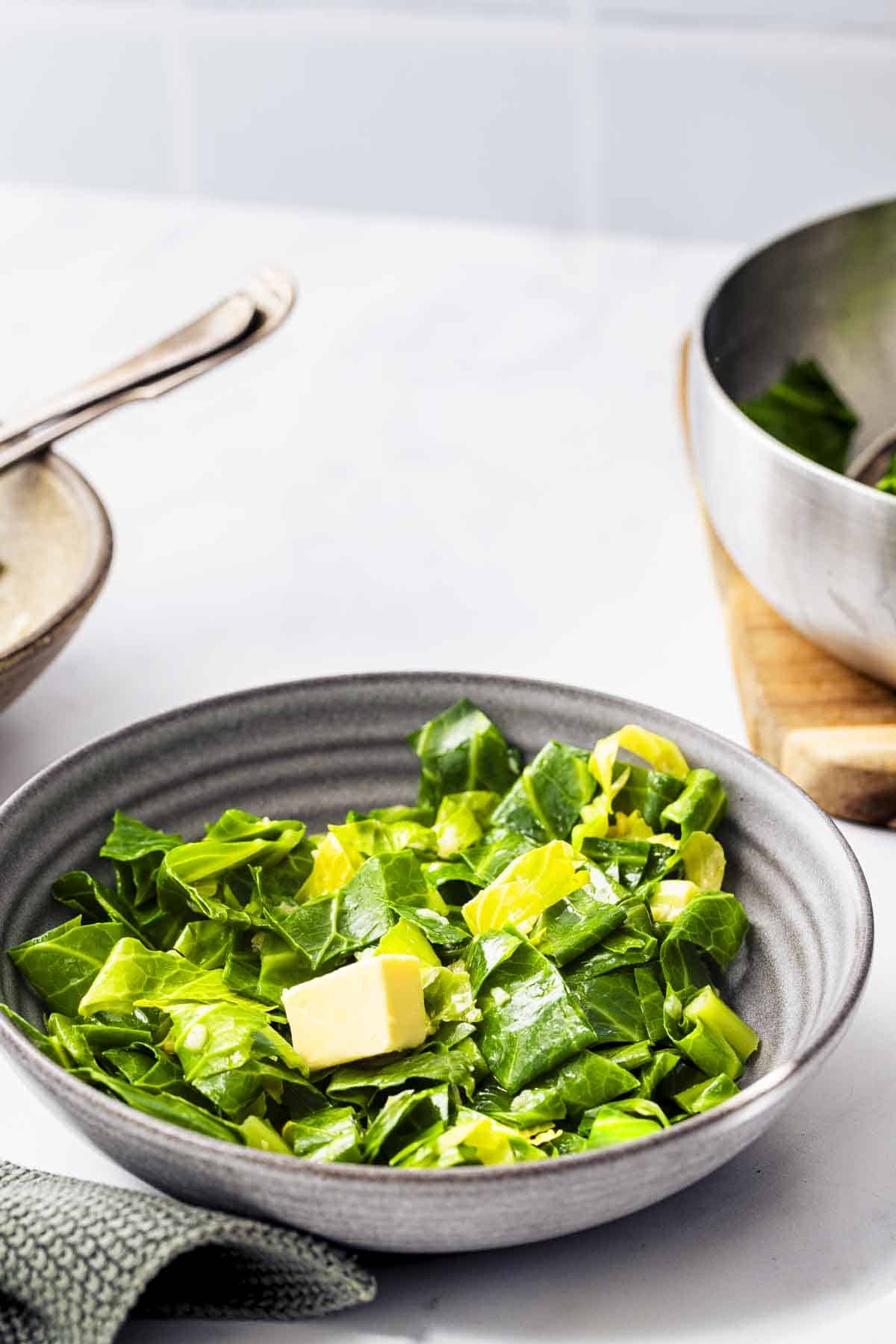 serving buttered spring greens in a grey bowl with a cube of butter.