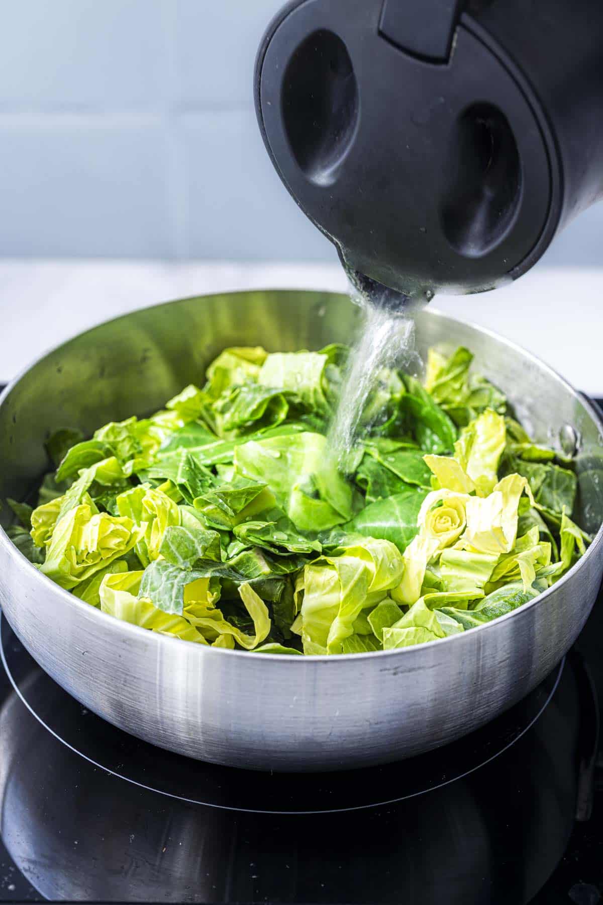 adding a kettle of boiling water to the spring cabbage in a pan.