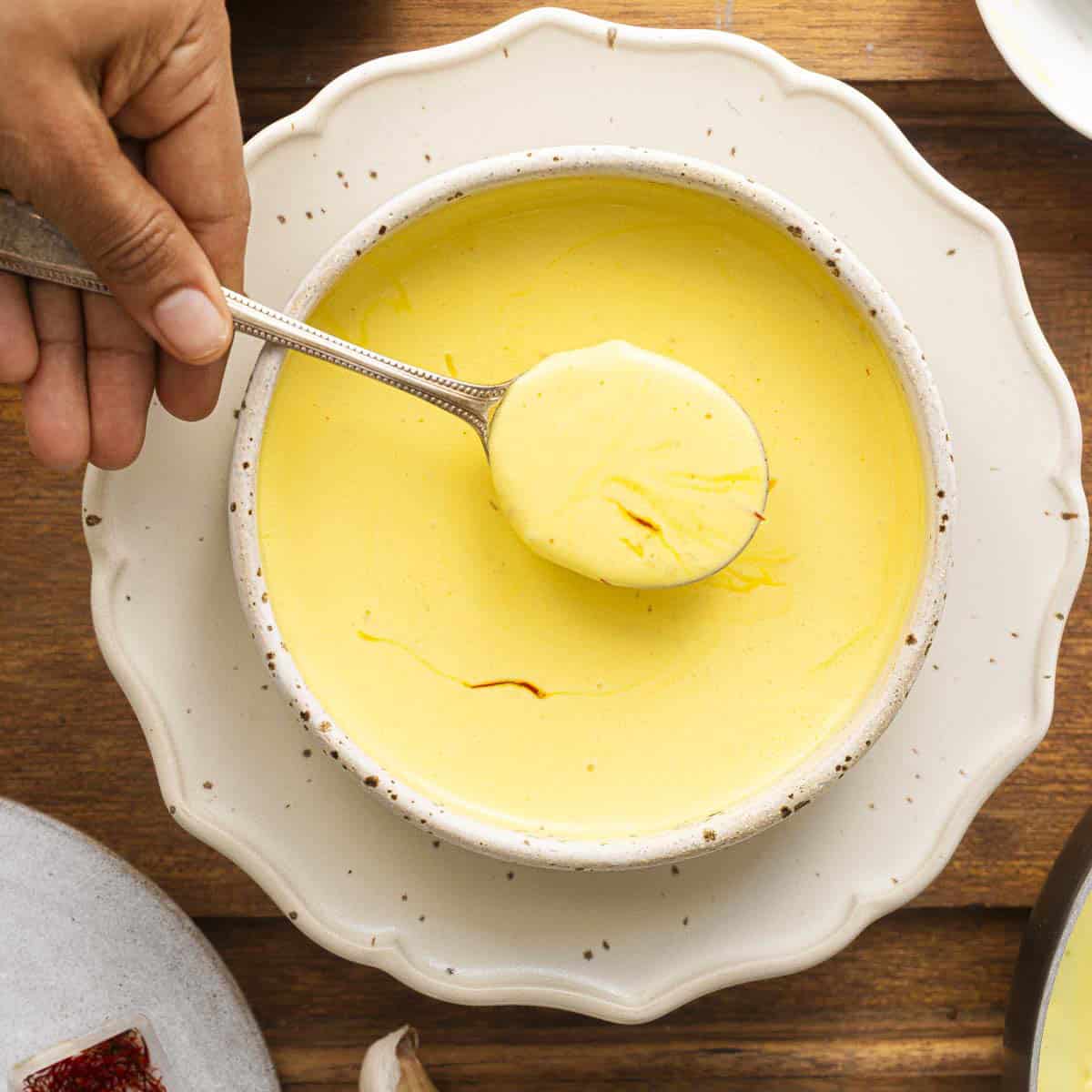 a bowl of saffron cream sauce in a white bowl. A lady holding a spoonful of creamy saffron sauce.