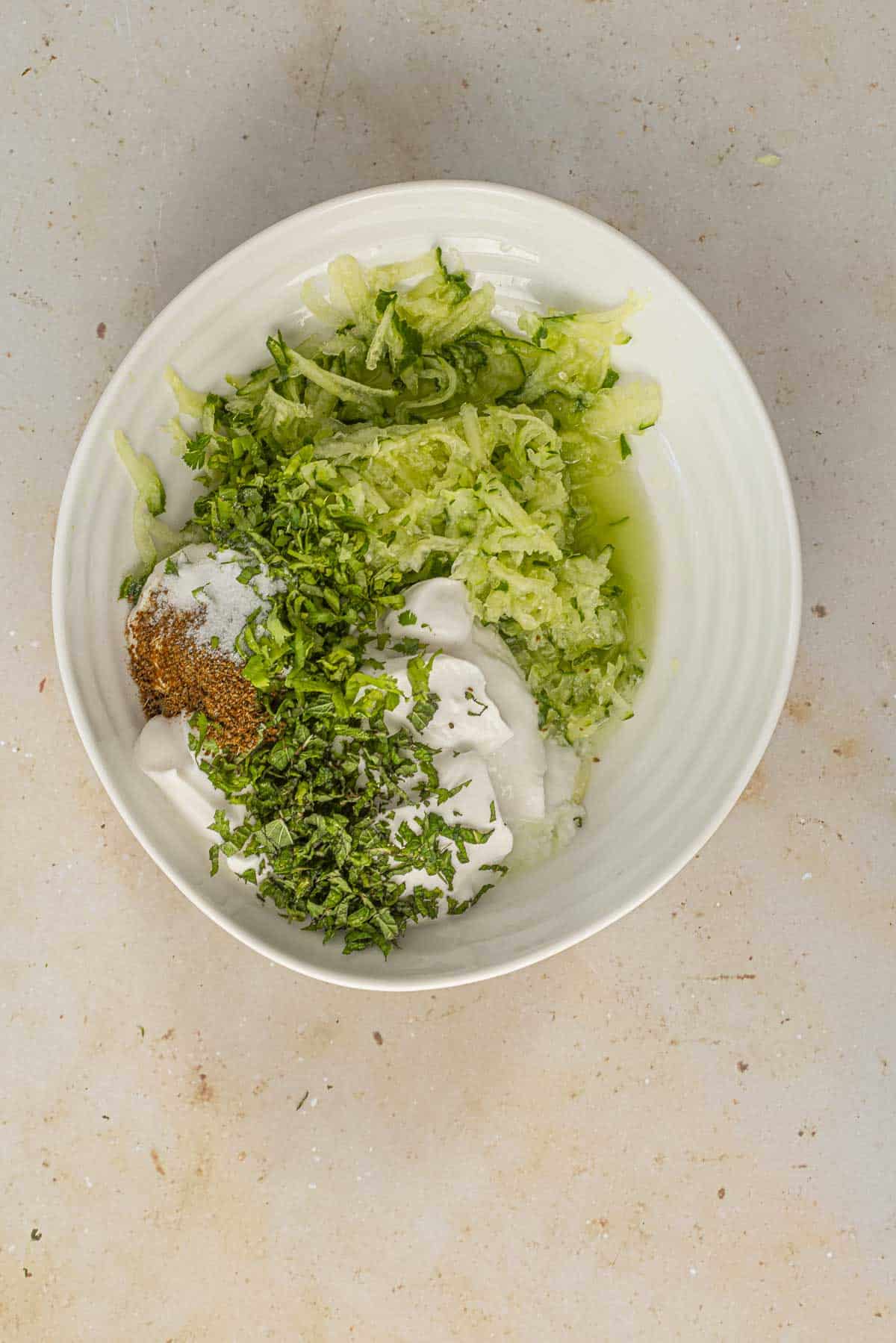 grated cucumber, yogurt, mint, coriander and spices in a white bowl.
