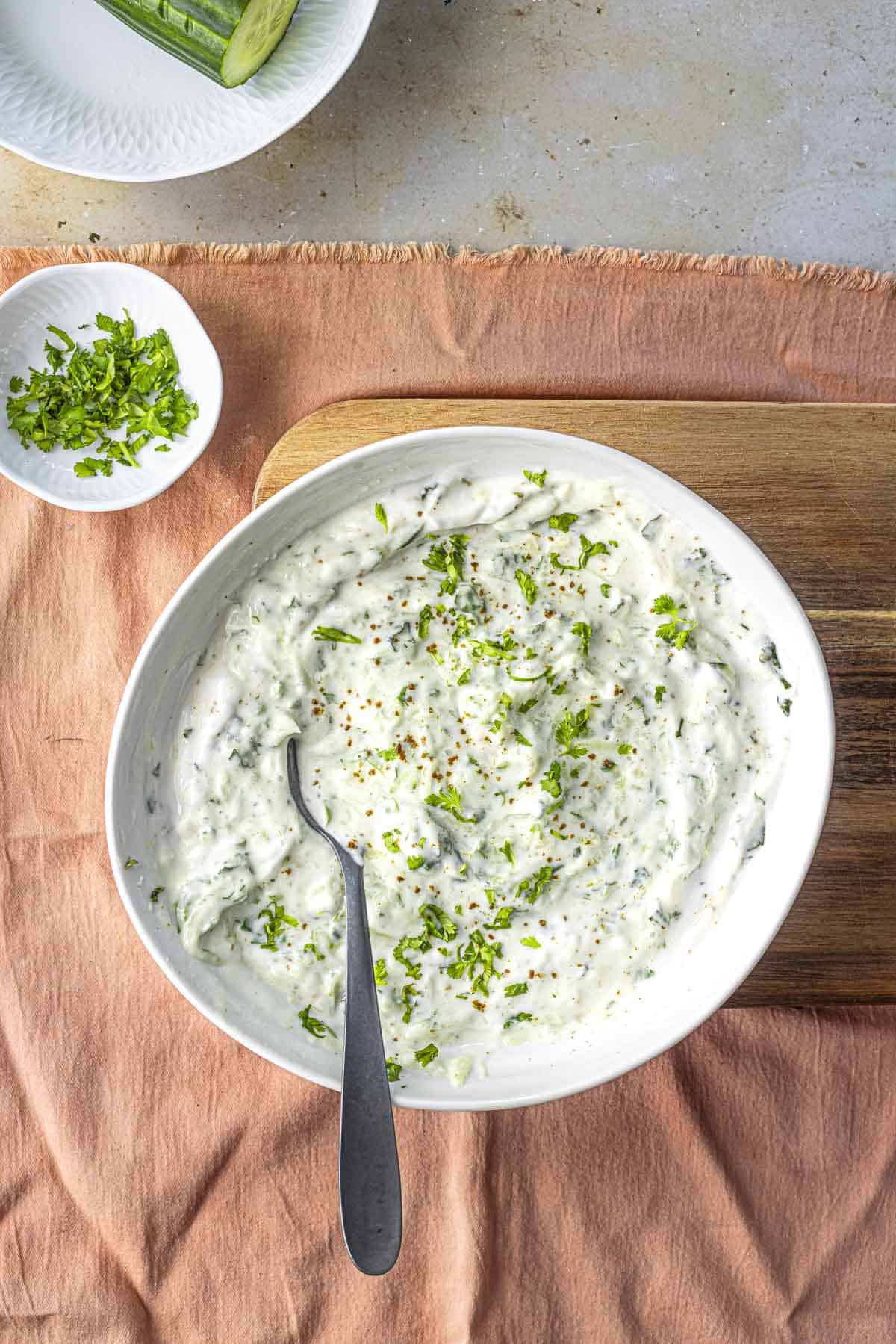 cucumber raita in a white bowl with a spoon.