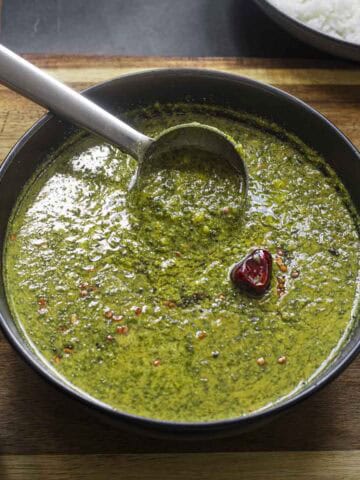a black bowl of spinach molagootal with a steel ladle.