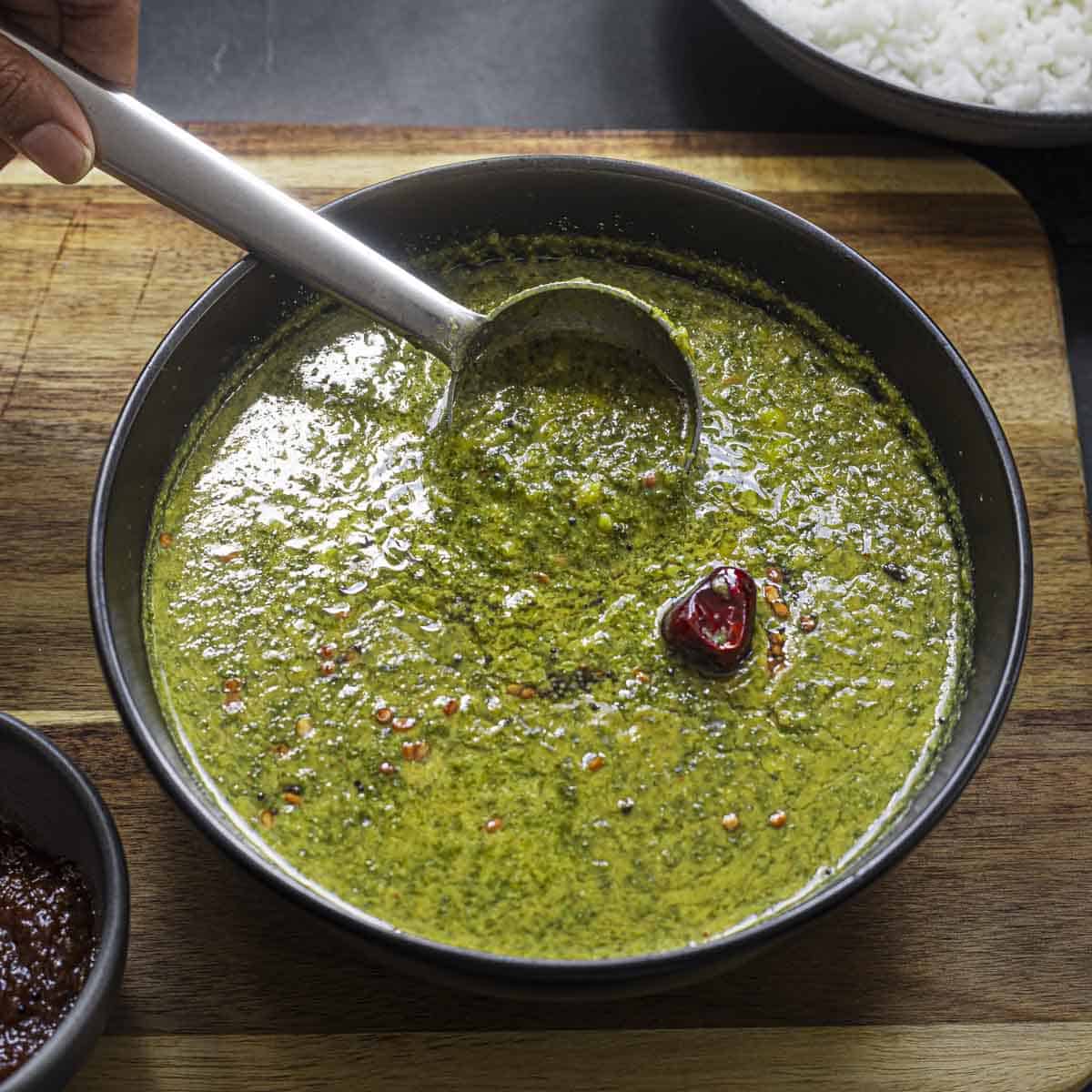 a black bowl of spinach molagootal with a steel ladle.