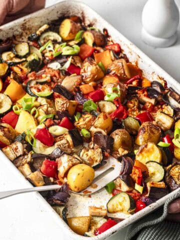 roasted summer vegetables bake in a tray with a spatula.