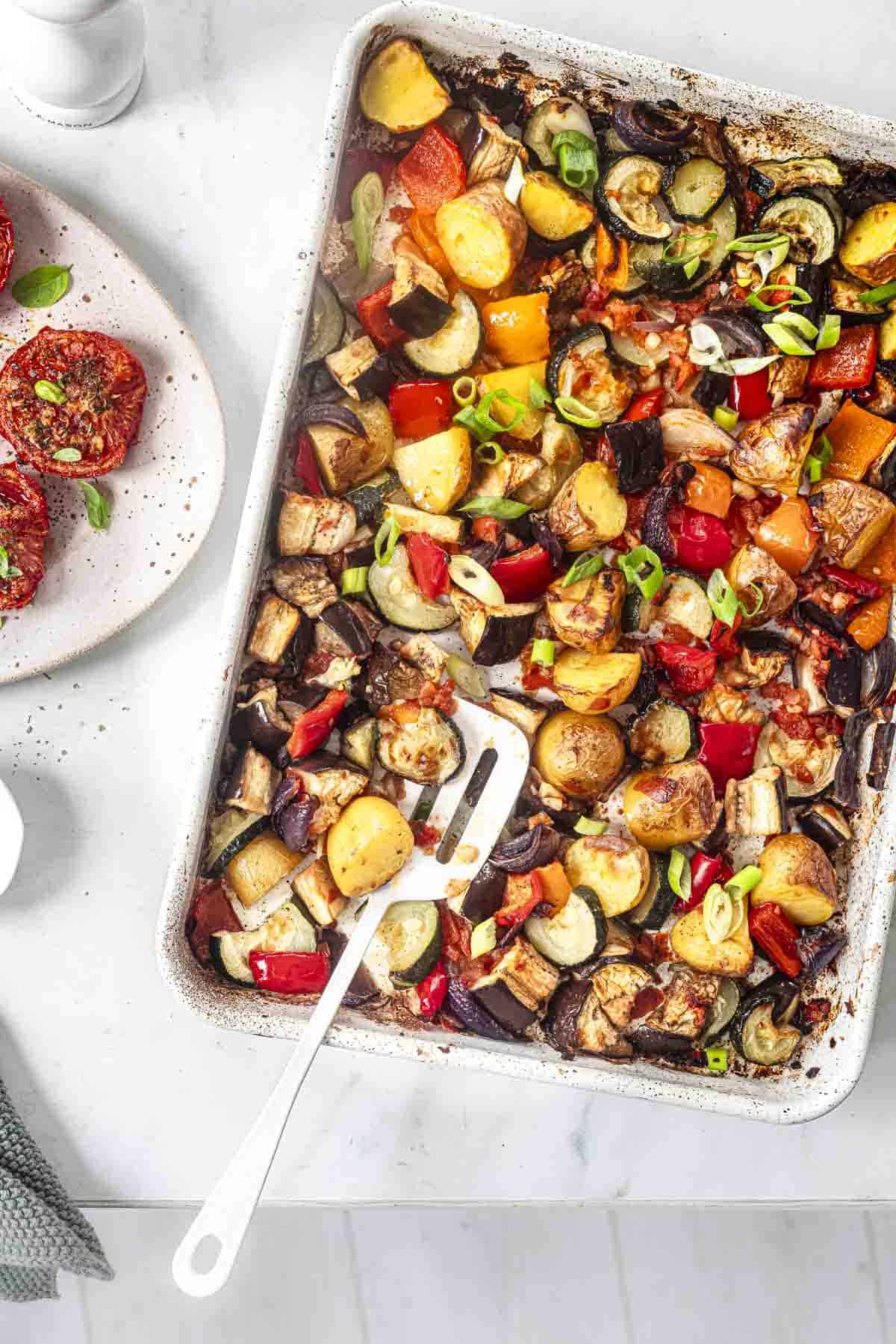 roasted summer vegetables in a tray bake alonh with roasted tomatoes in an oval dish.