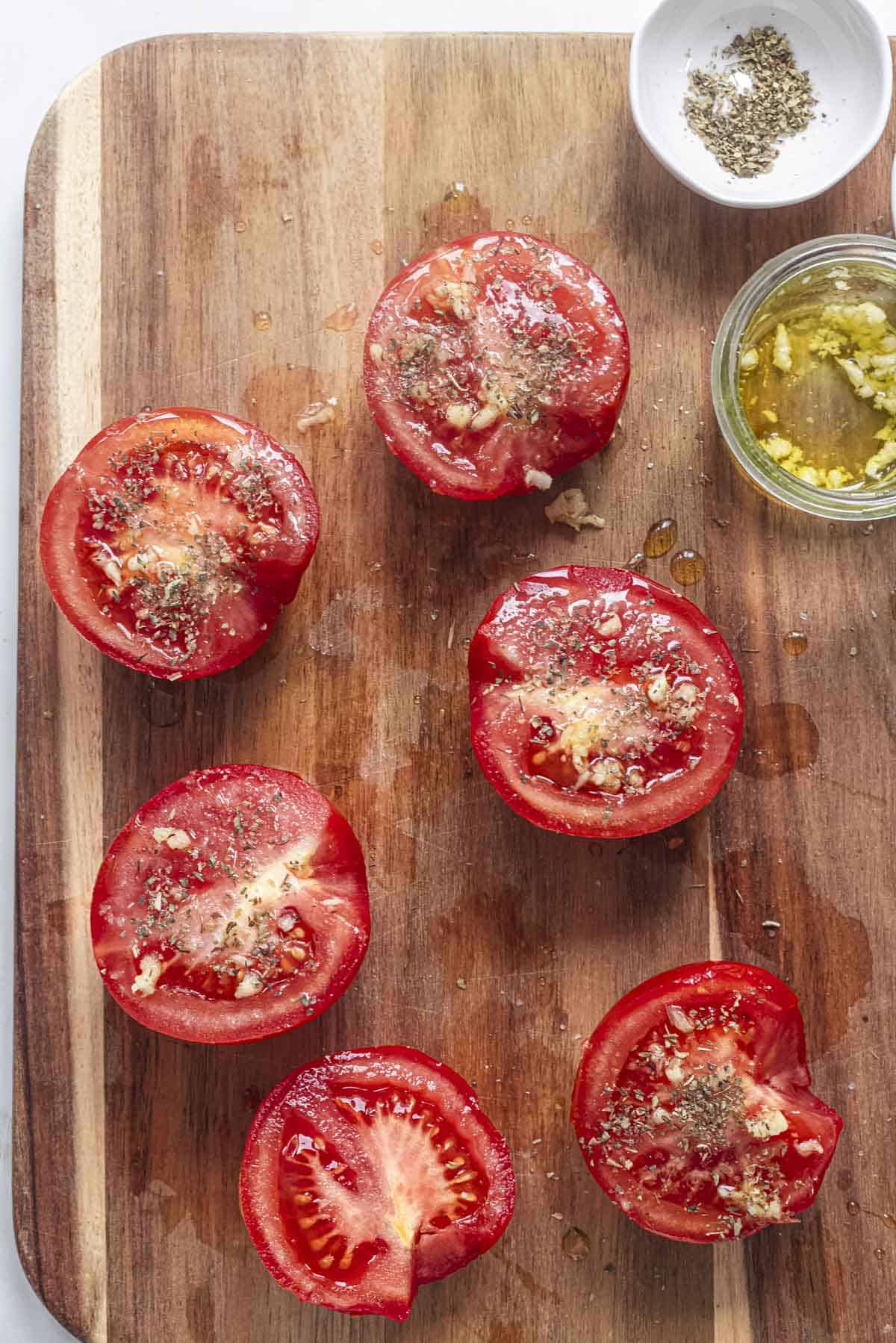 halved tomatoes seasoned with garlic and Italian seasoning on a chopping board.