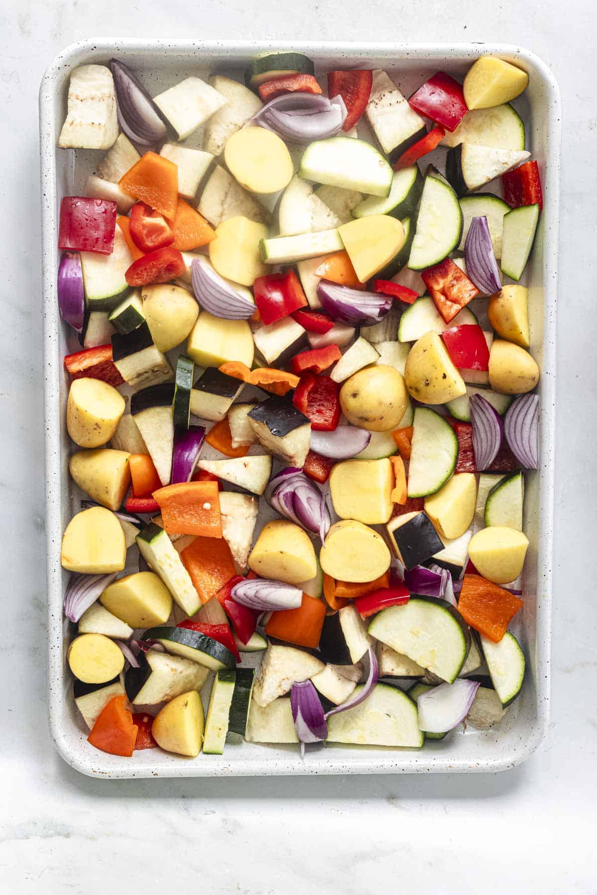 aubergine, courgette, potato, pepper and onion in a white baking sheet to make summer traybake.