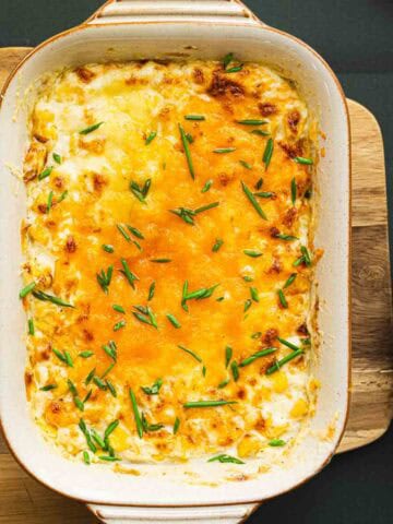 creamy christmas corn garnished with chives on a wooden board.