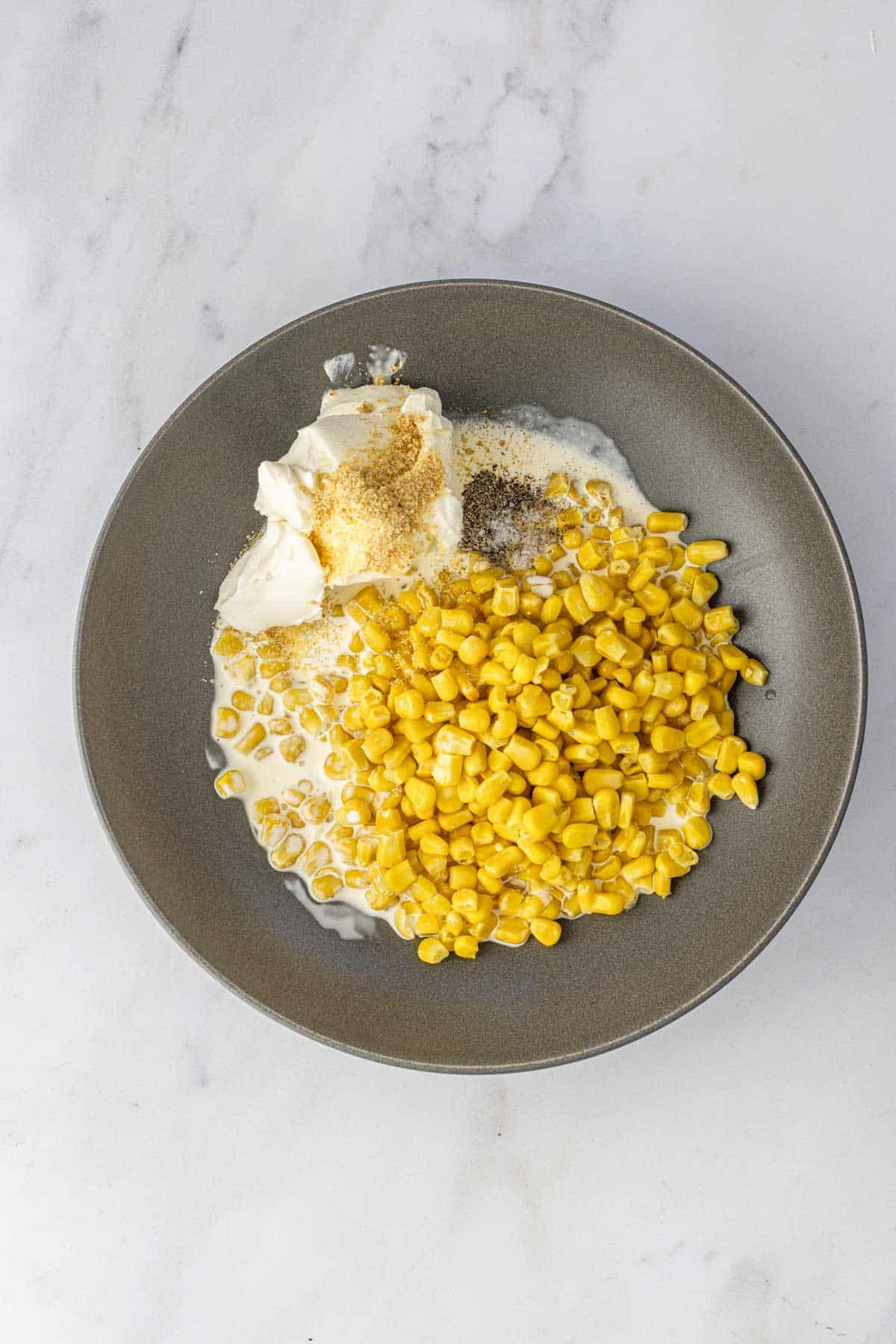 sweet corn, cream, cream cheese and seasoning in a grey bowl to make christmas corn.