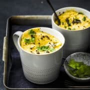 Two mug khaman dhoklas served with garnishes.