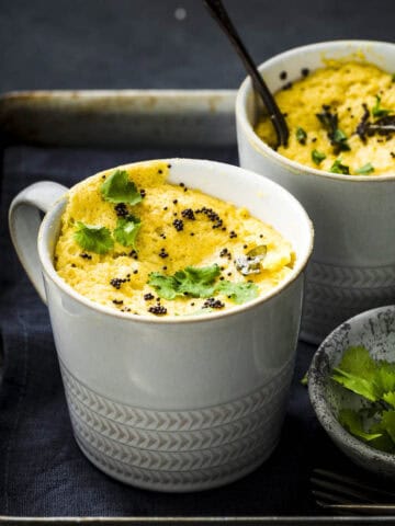 Two mug khaman dhoklas served with garnishes.