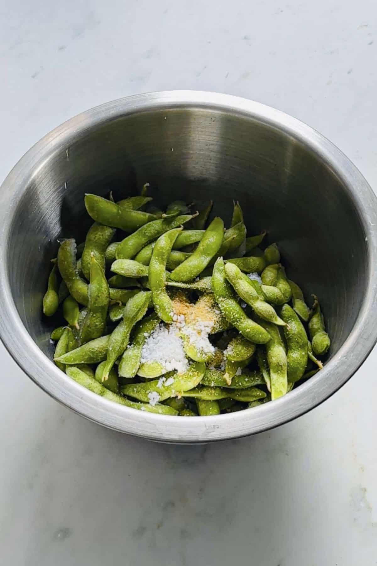 frozen edamame pods with seasoning in a mixing bowl.