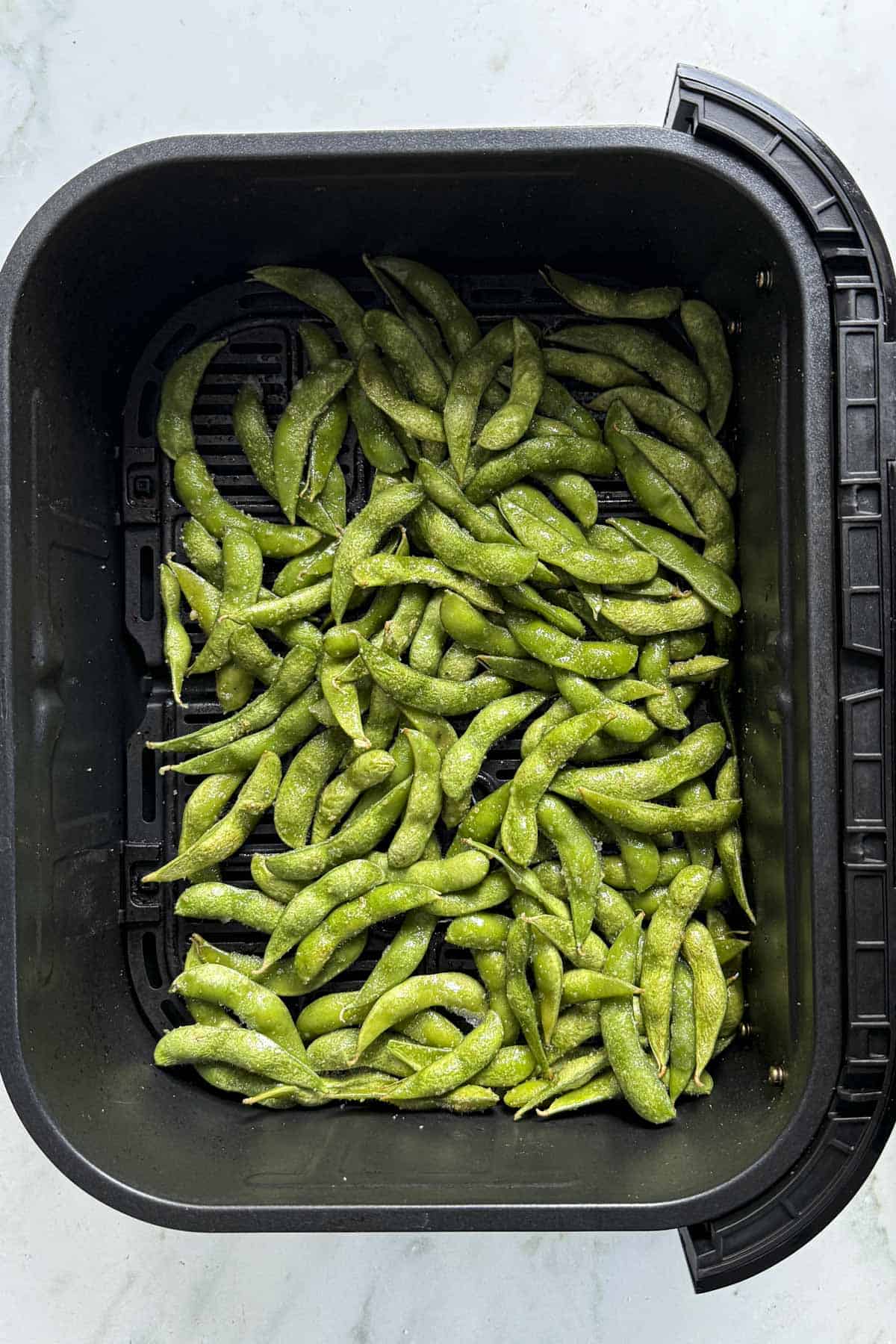 seasoned edamame in air fryer basket for air frying.