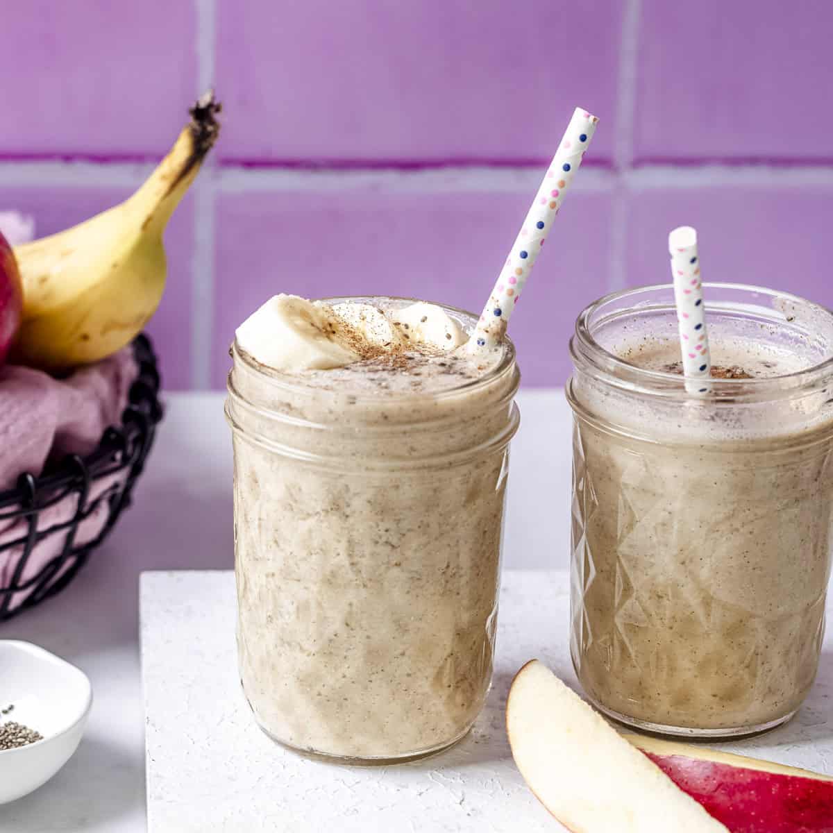 two mugs of vegan apple banana smoothie served with banana toppings.