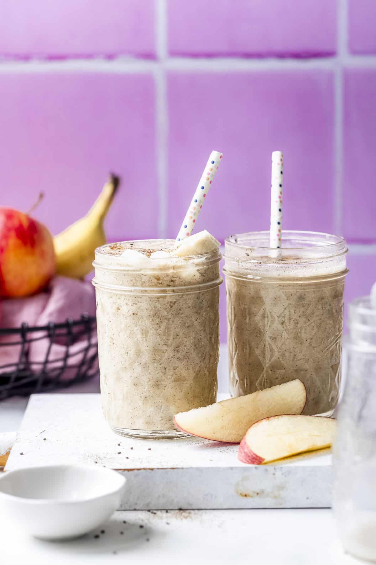 two mugs of vegan apple banana smoothie served with sliced banana topping.