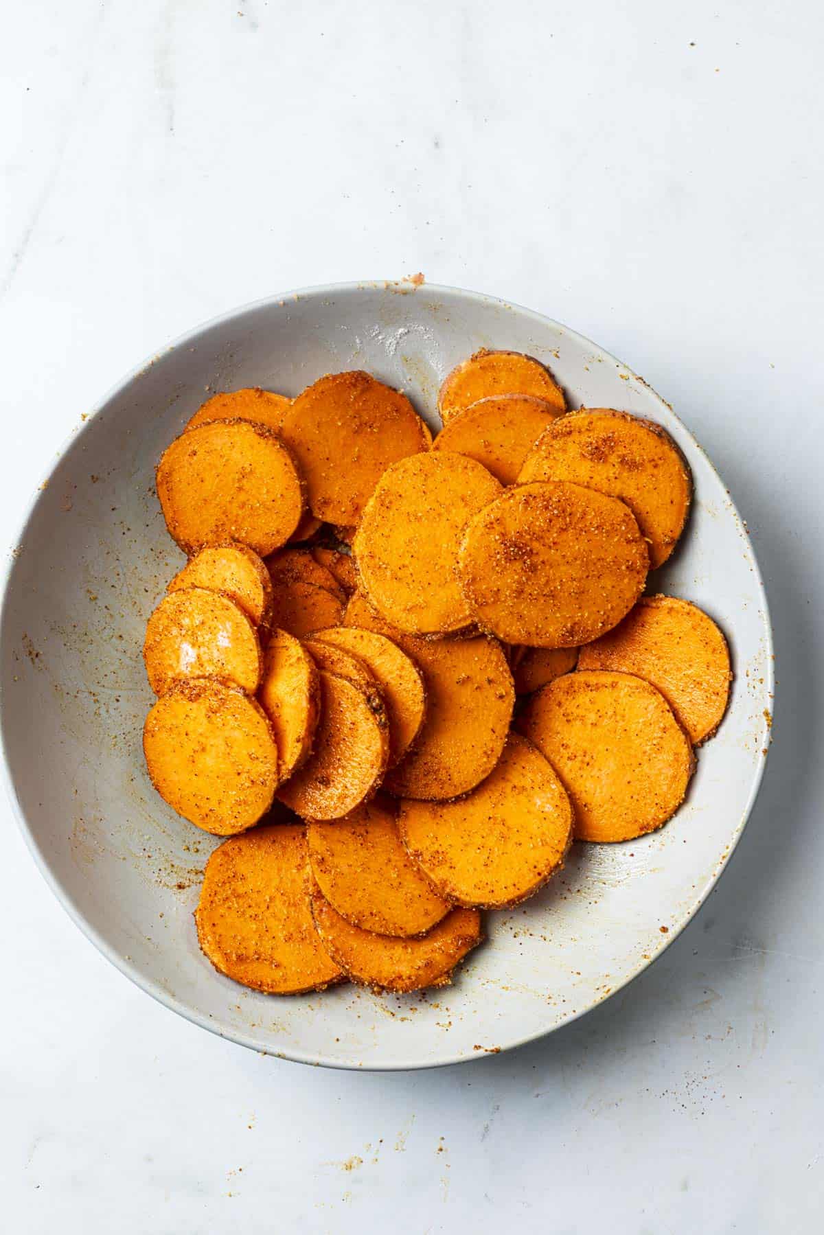 spice coated sweet potato round slices in a bowl.