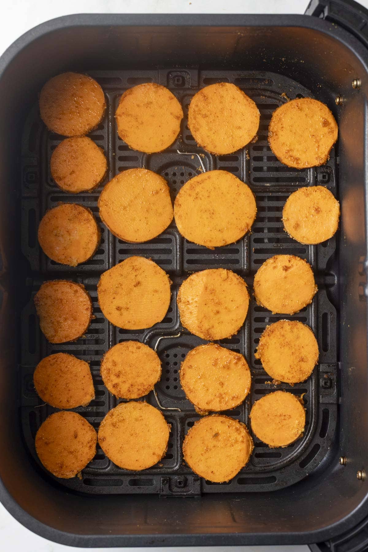 spice coated sweet potato slices arranged in air fryer basket.