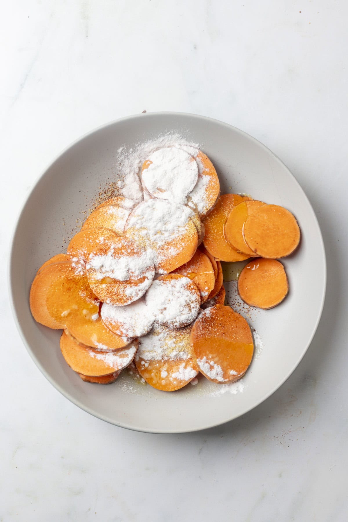 sliced sweet potato rounds with spices and rice flour in a bowl.