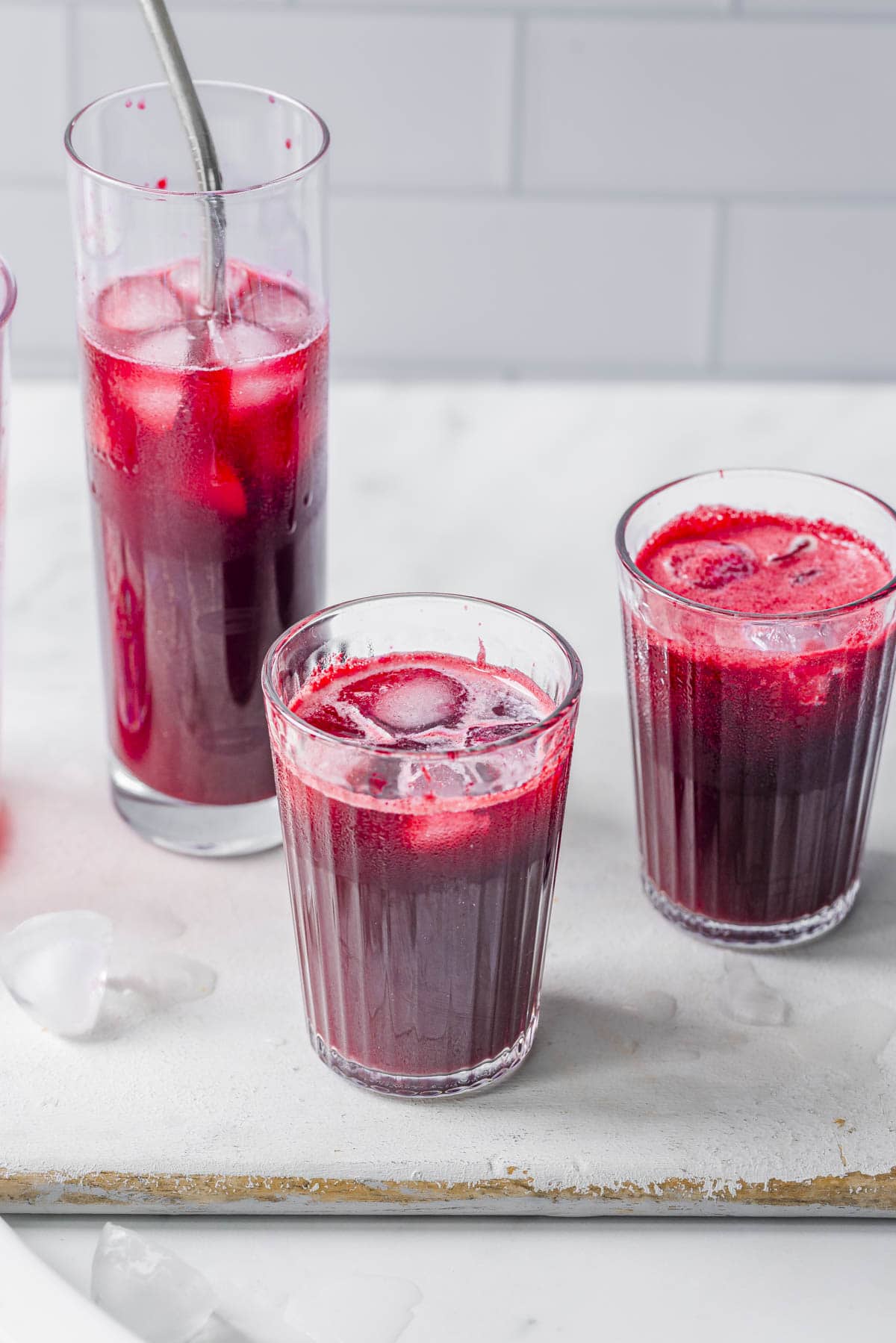 Three glasses of freshly pressed slow juicer beet apple, and ginger juice served over ice.
