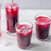 Three glasses of freshly pressed slow juicer beet apple, and ginger juice served over ice.