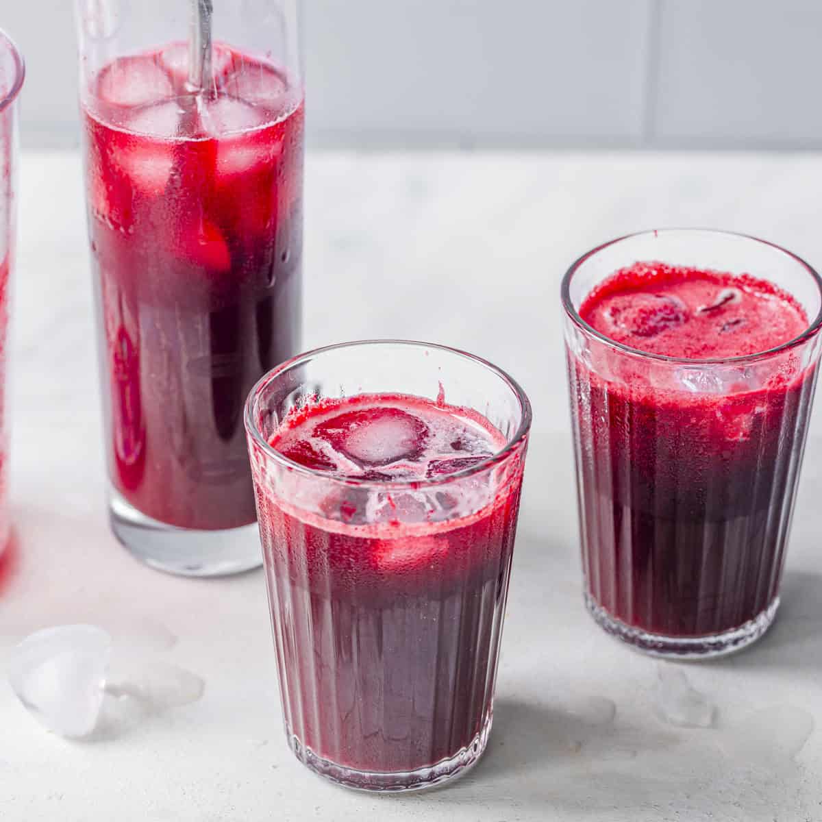 Three glasses of freshly pressed slow juicer beet apple, and ginger juice served over ice.