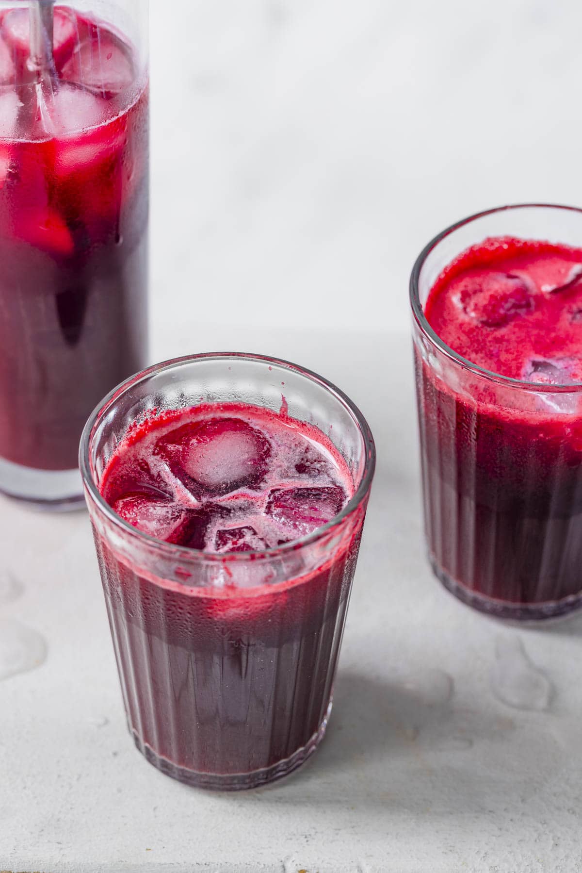 Three glasses of freshly pressed slow juicer beet apple, and ginger juice served over ice.
