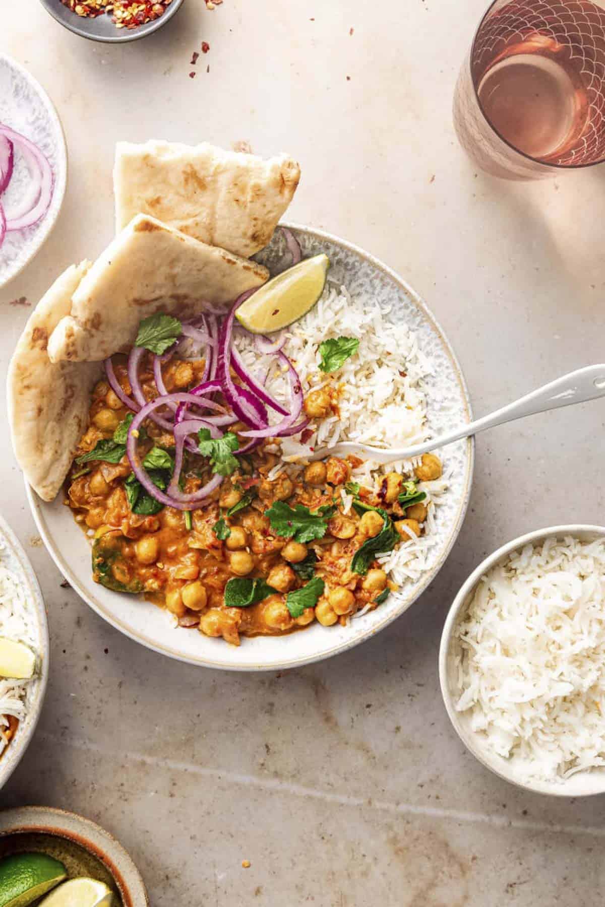 two bowls of easy vegan chickpea spinach curry served with rice and naan.