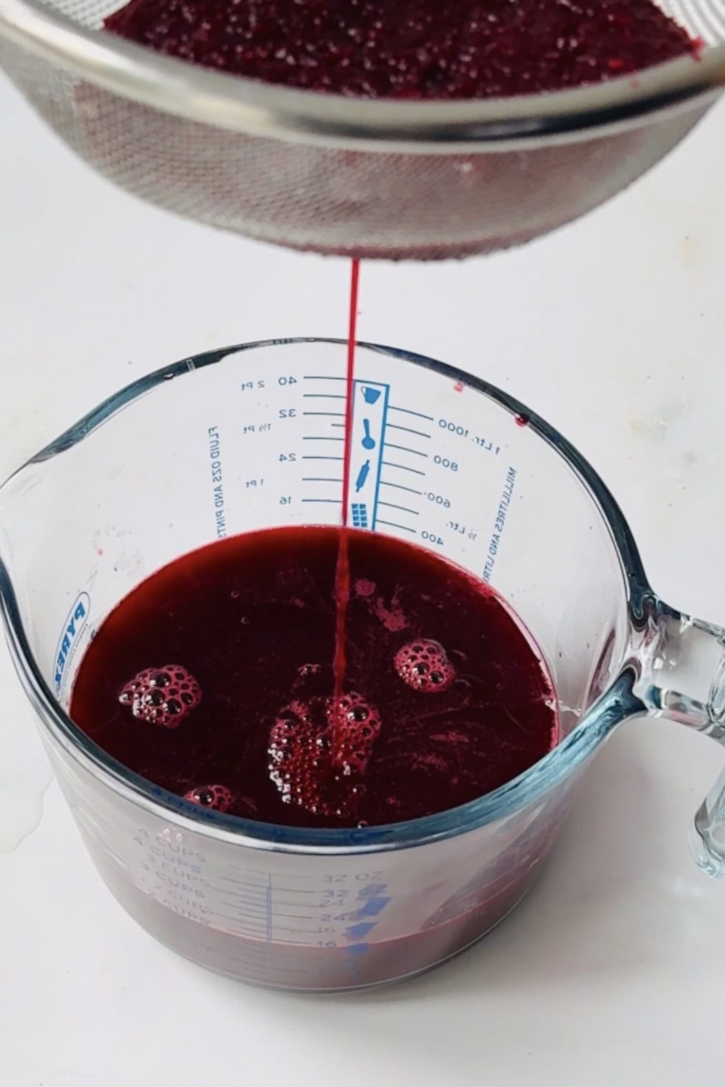 Straining beetroot ginger juice in a glass bowl.