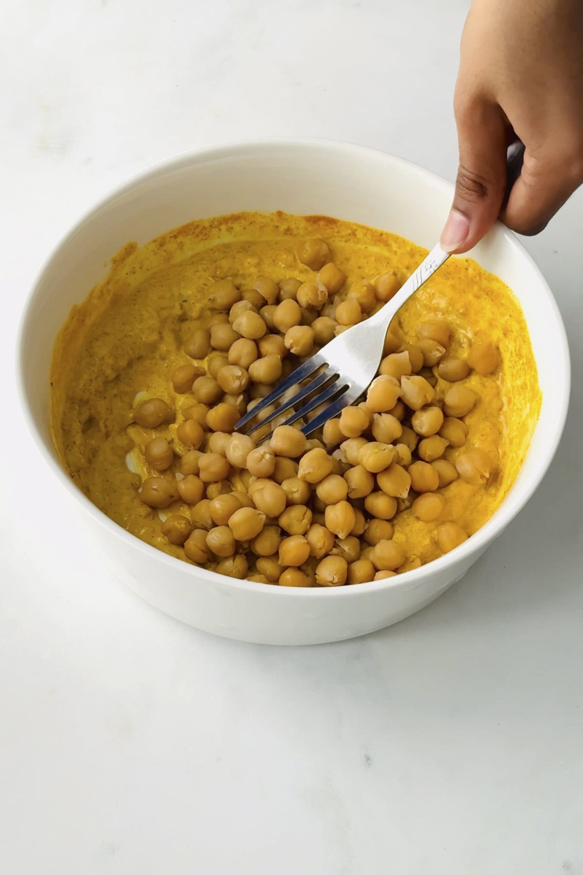 mashing the chickpeas with a fork in a white bowl.