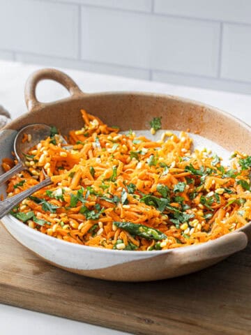 a bowl of moong dal carrot kosambari salad in a bowl with two spoons.