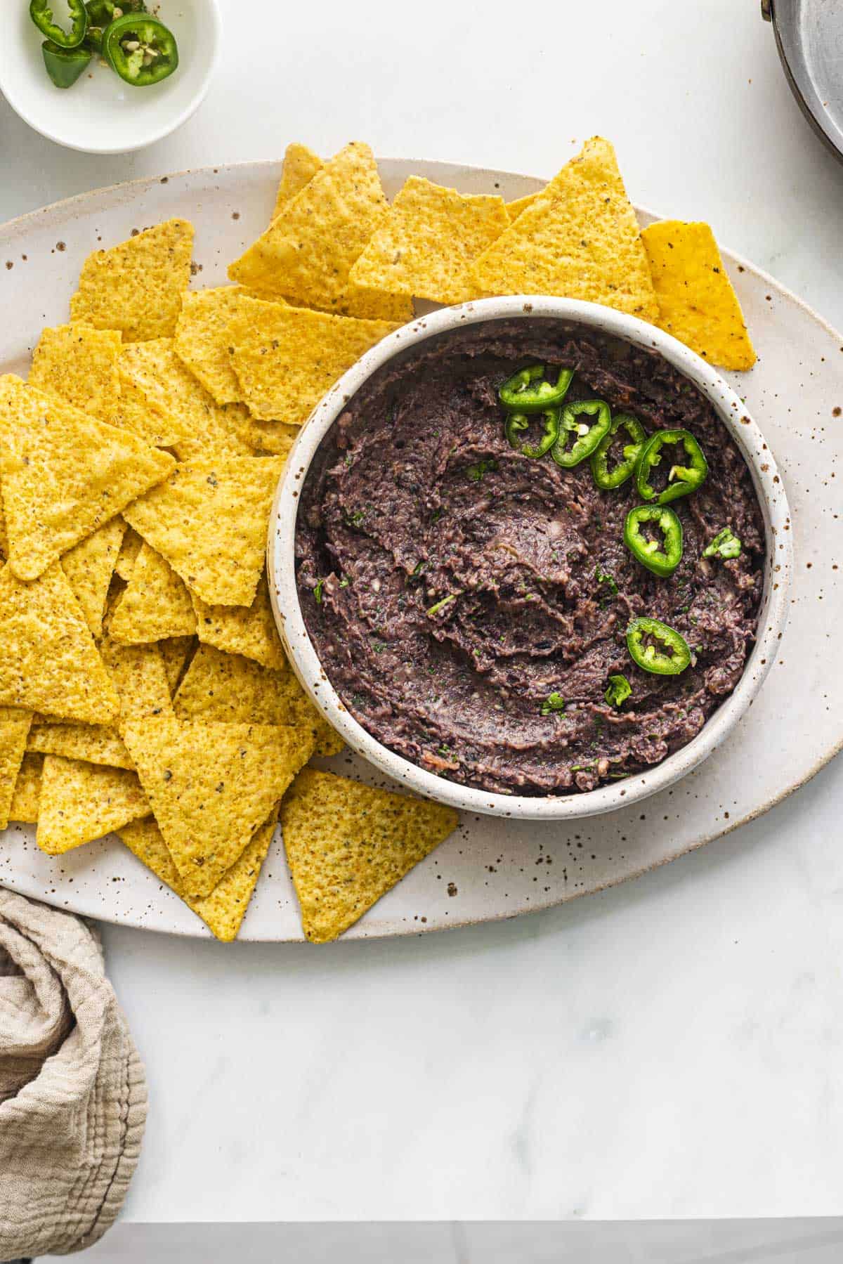 a white bowl of quick and easy spicy  black bean dip served with tortilla chips.
