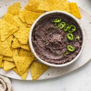 a white bowl of quick and easy spicy black bean dip served with tortilla chips.