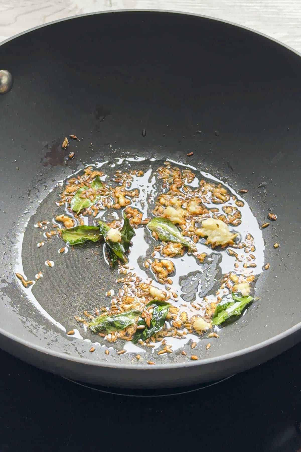indian tempering with garlic, cumin and curry leaves for red lentil dal in a wok.