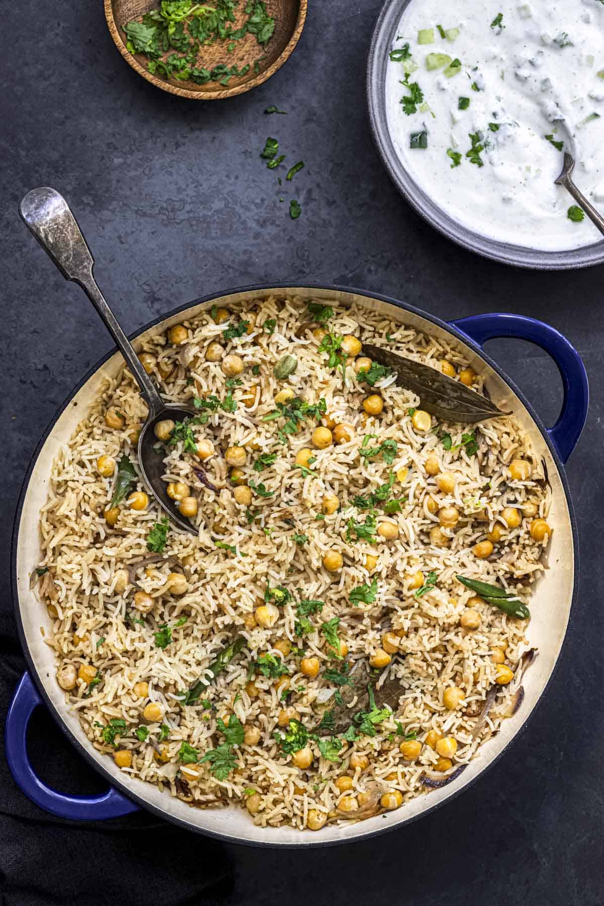 chickpea pulao in a deep pan served with cucumber raita in the side.