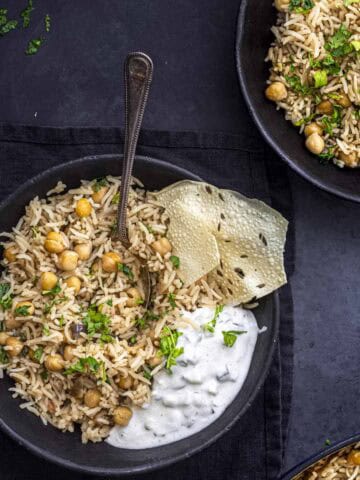 two bowls of chana pulao served with raita and papad.