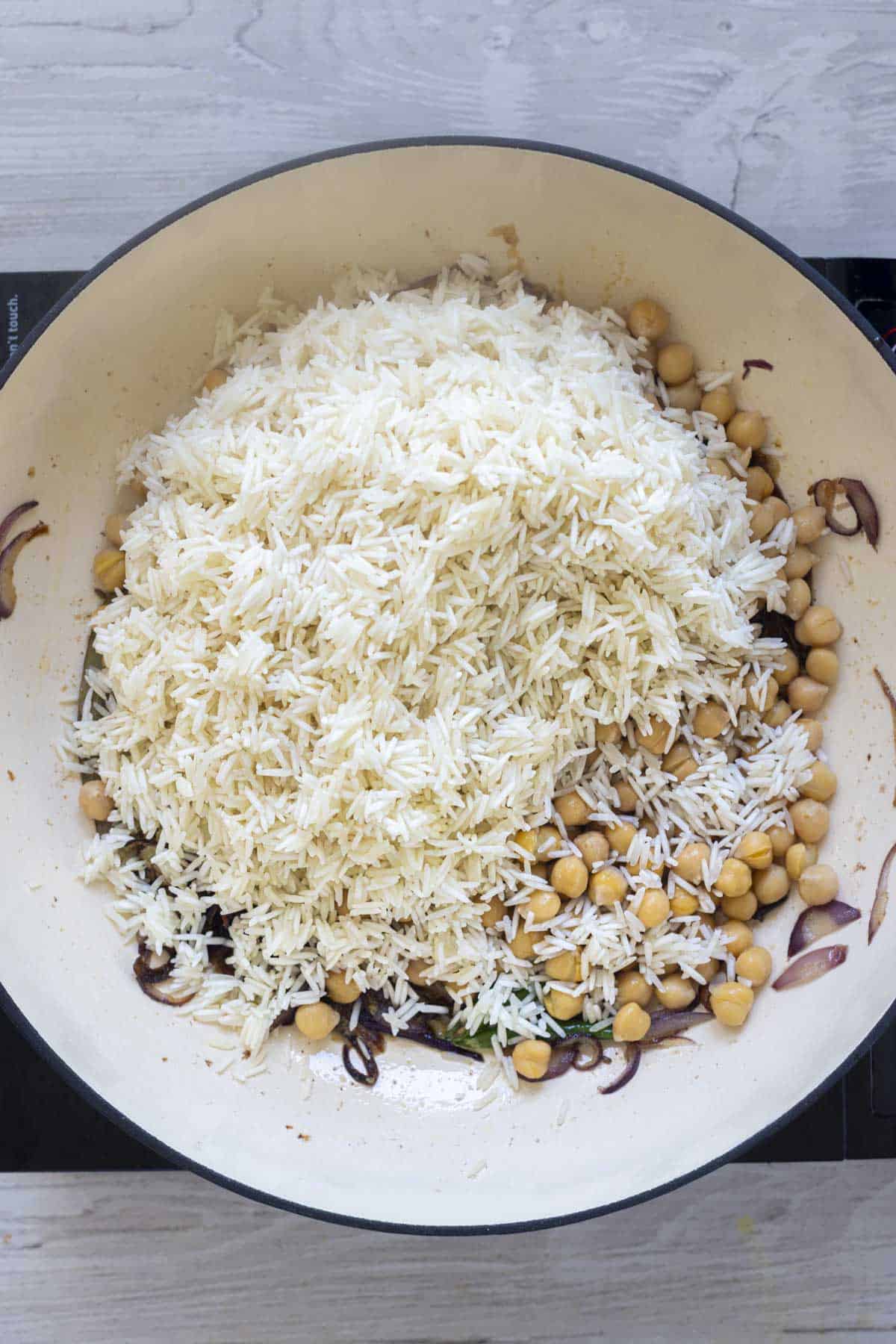 rice and chickpeas in a deep pan to make pulao rice.