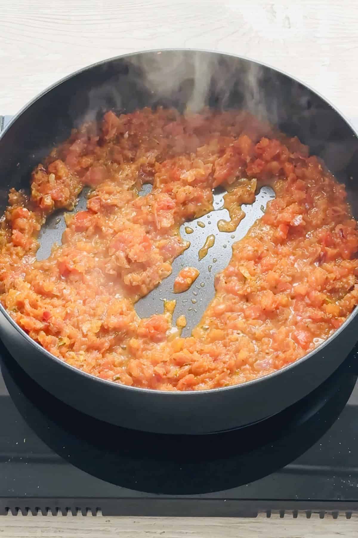 onion tomato masala cooking in a black saute pan.