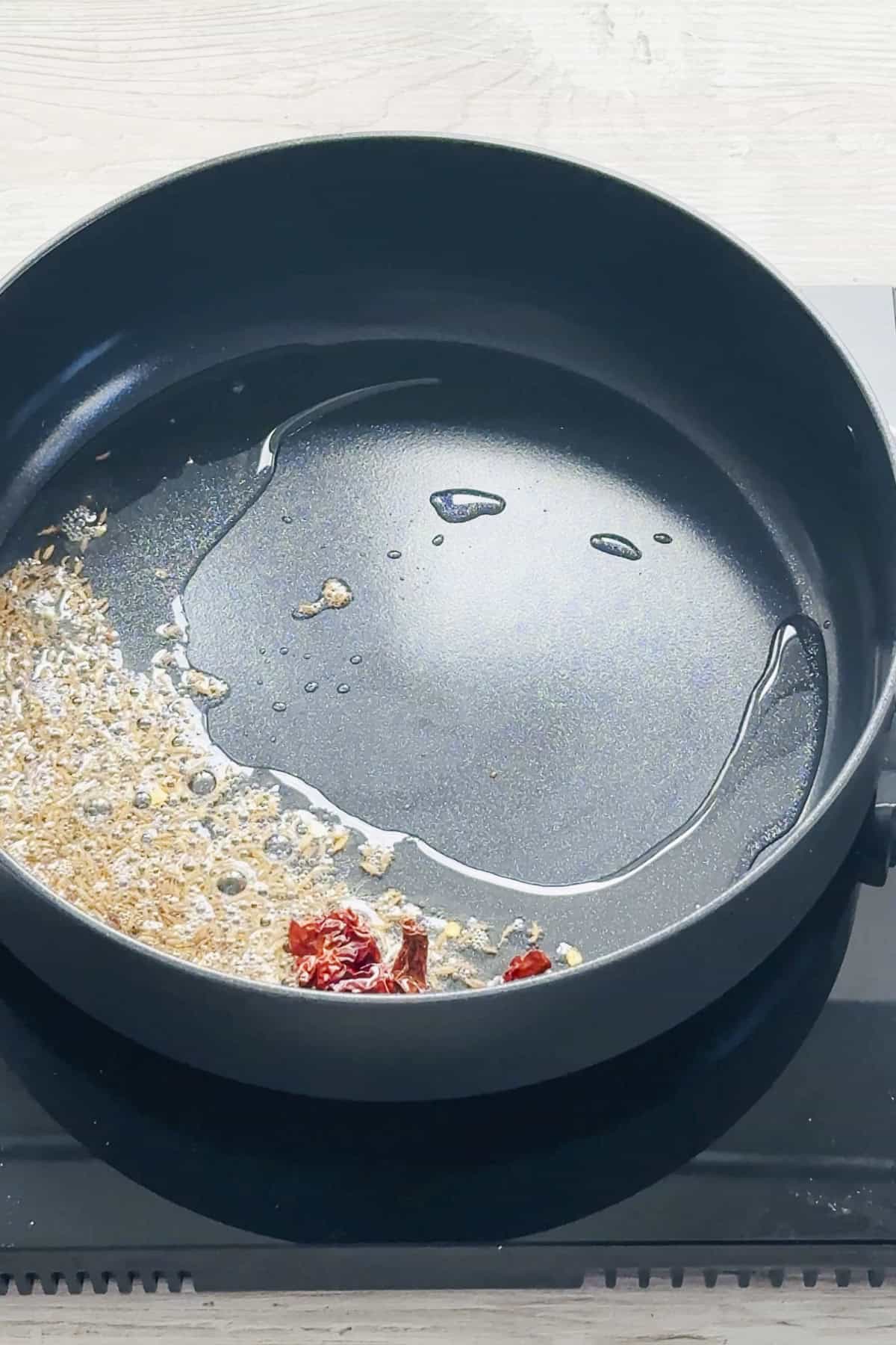 Oil, cumin seeds and red chilli in a saute pan.